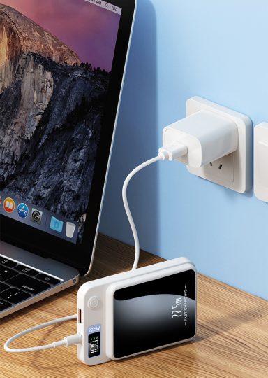 Un smartphone blanc en charge, connecté à un ordinateur portable et à une prise murale.