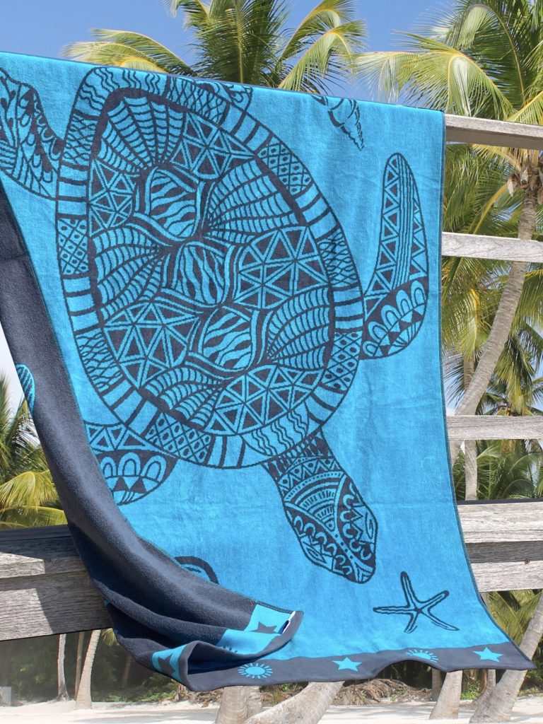 Serviette de plage turquoise ornée d'une tortue et d'une étoile de mer sur une balustrade en bois.